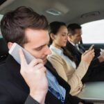 Business professionals multitasking with phone and tablet in car, illustrating productivity on the go.